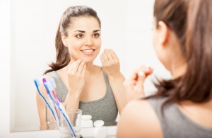 Portrait of a young woman standing in front of a mirror in the bathroom and cleaning her teeth with dental floss